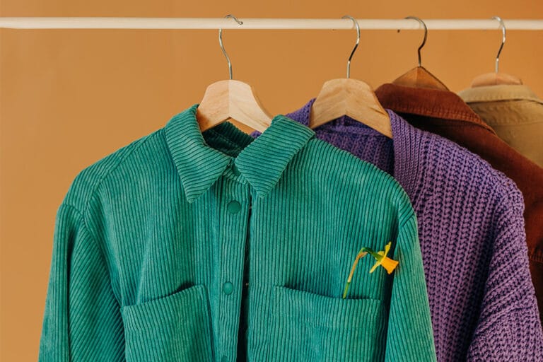 Green corduroy shirt on hanger with flower in pocket – purple and brown garments in background.