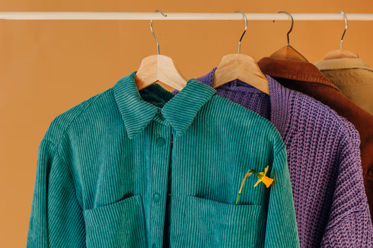Green corduroy shirt on hanger with flower in pocket – purple and brown garments in background.