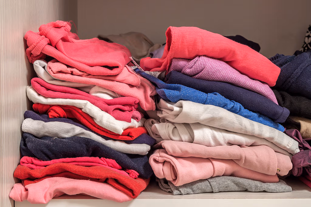 Neatly stacked piles of folded clothes in shades of red, pink, blue, and white.