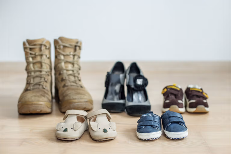 Four pairs of shoes including boots, high heels, and children’s footwear arranged on a wooden floor.