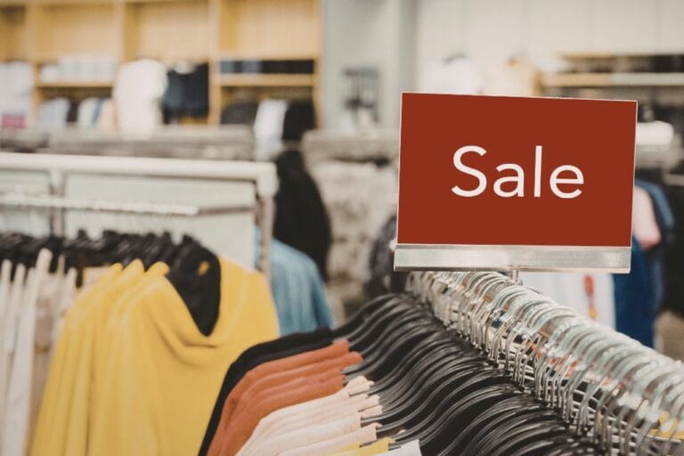 A clothes shop showing different coloured jumpers on a rail with a red "Sale" sign ono top.